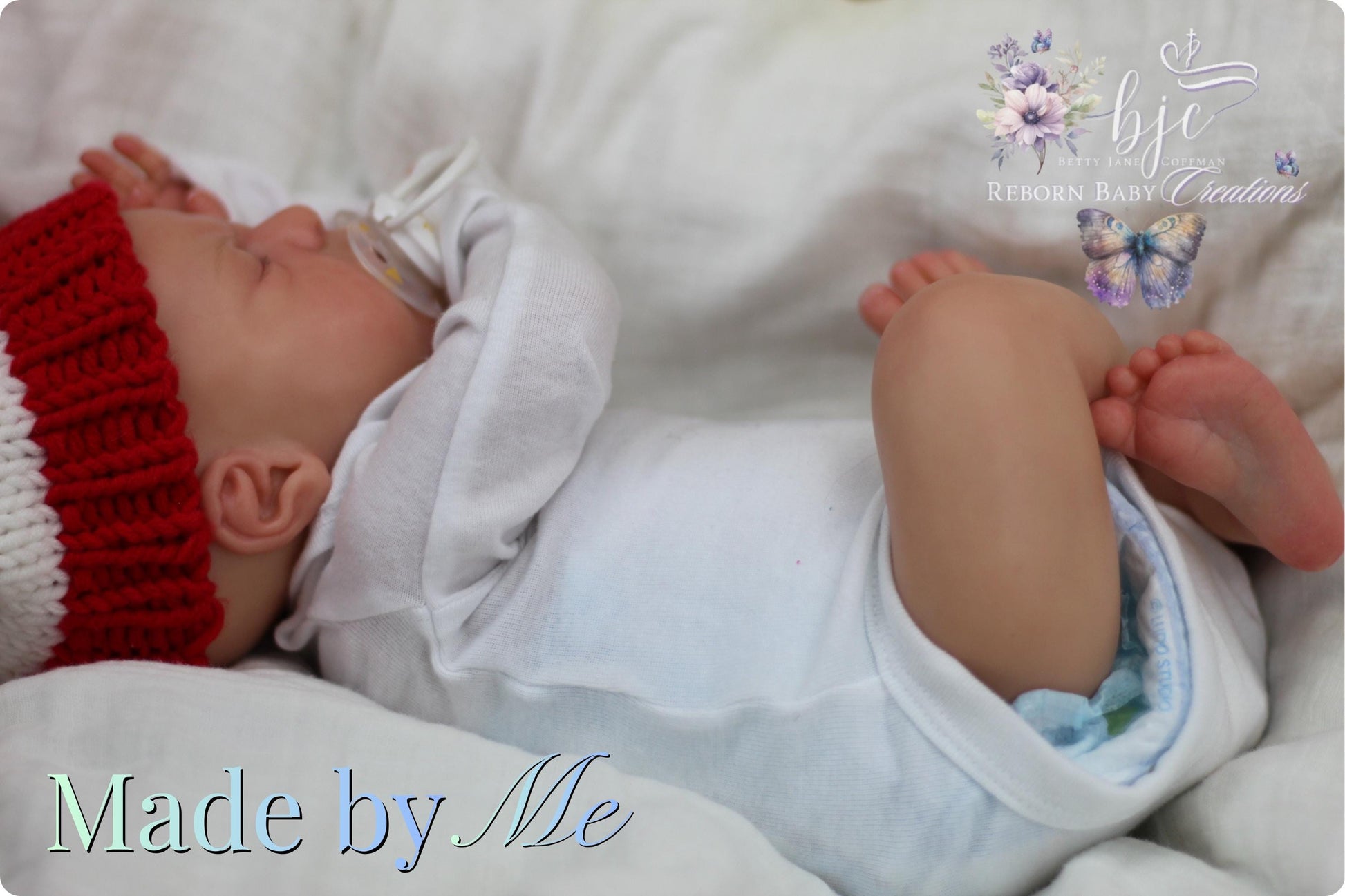 A newborn baby lying on a bed, wearing a white onesie and a red knit hat.