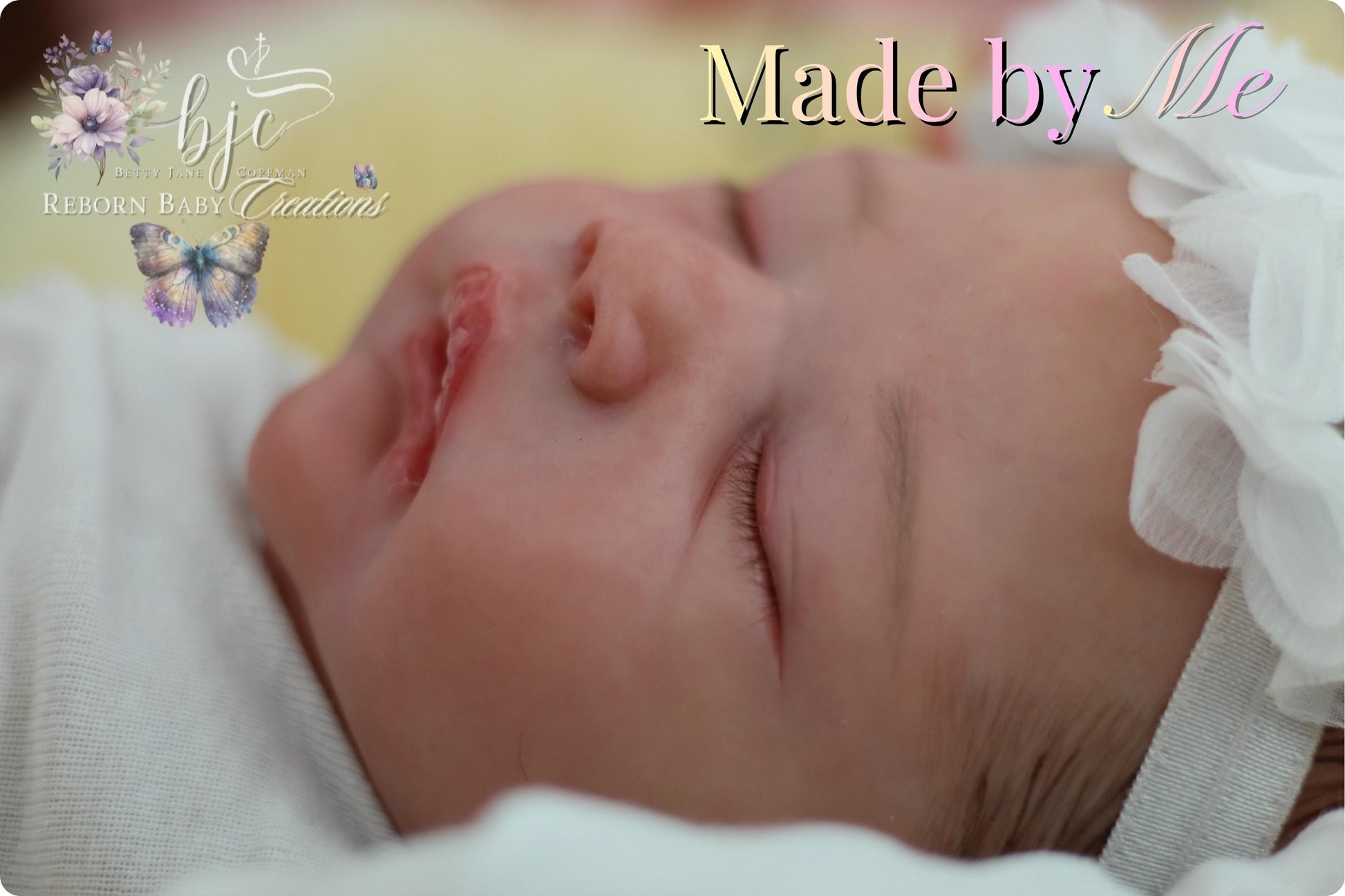 A newborn baby is peacefully sleeping, with a white flower headband and a butterfly design on the blanket.