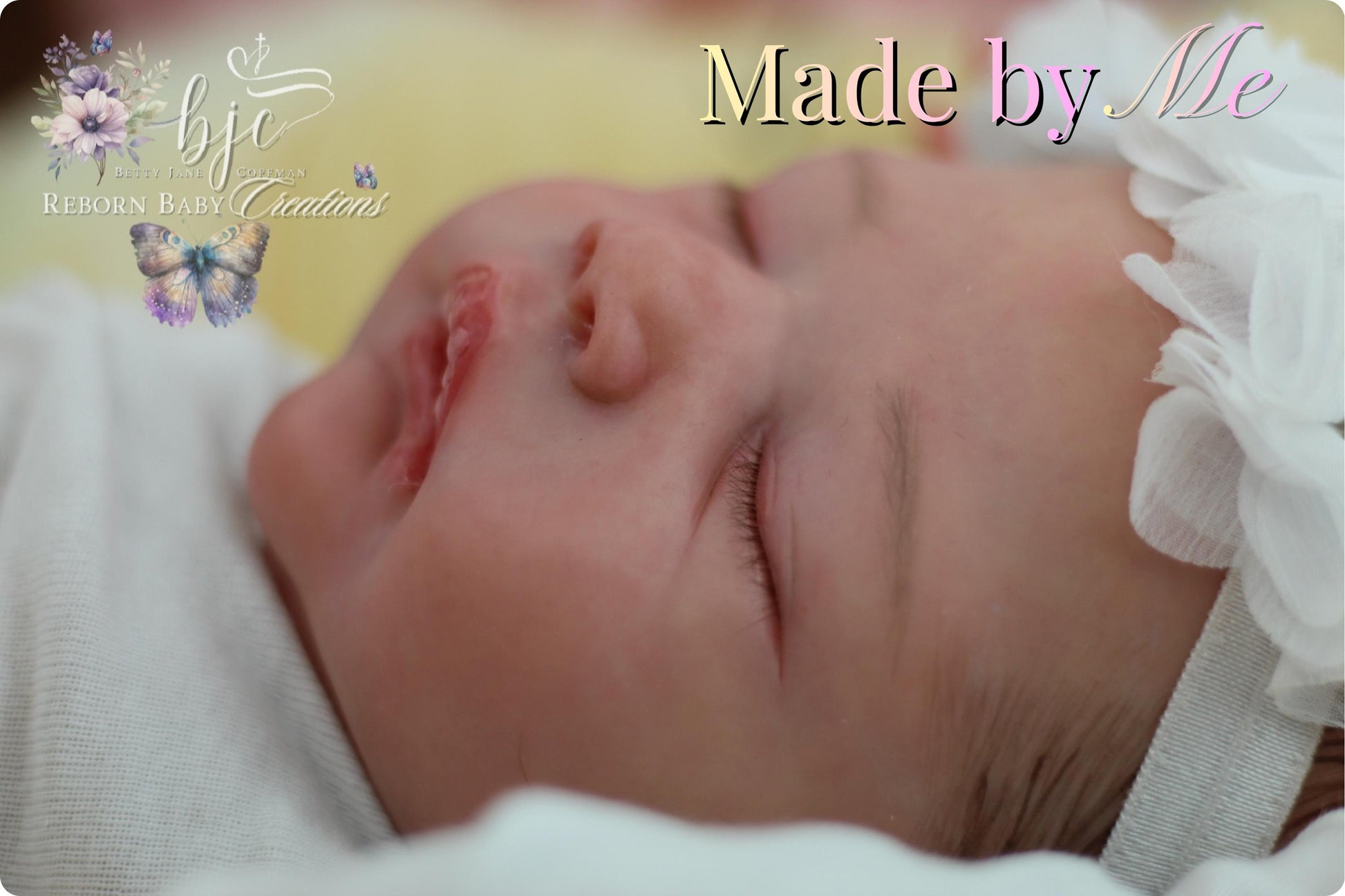 A newborn baby is peacefully sleeping, with a white flower headband and a butterfly design on the blanket.