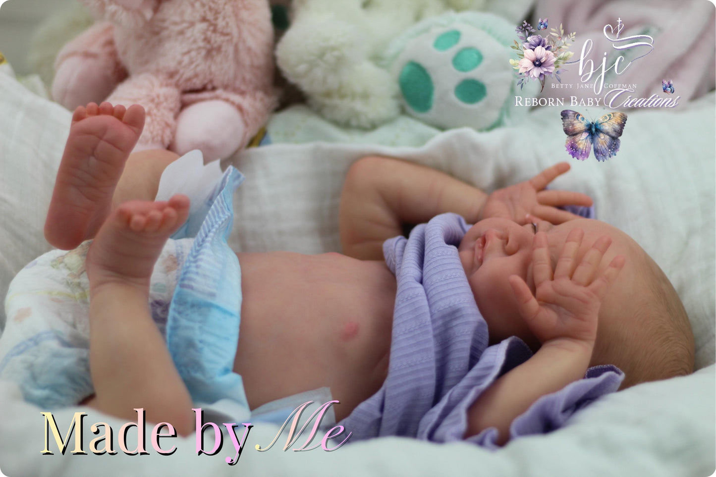 A newborn baby lying on a bed, wearing a purple blanket and surrounded by stuffed animals.