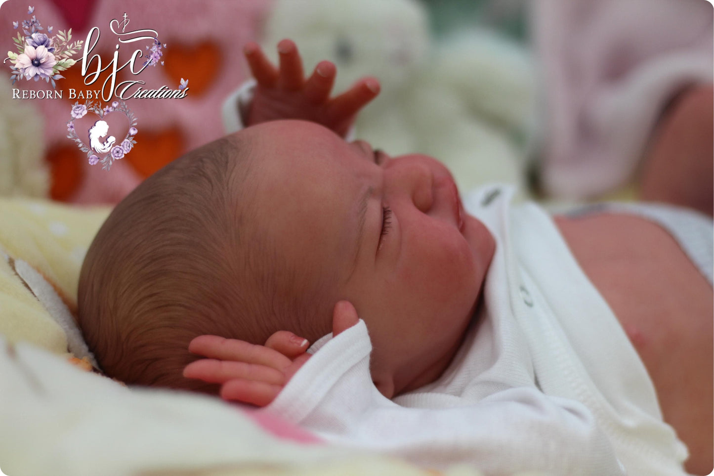 A newborn baby lying on a bed, with their hands reaching up towards the camera.