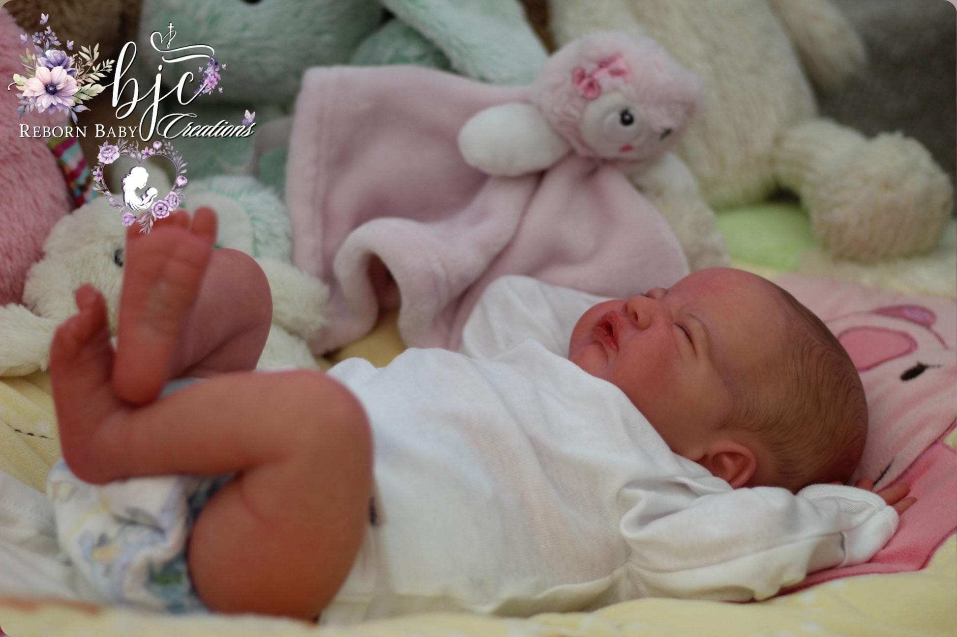 A newborn baby lies peacefully on a bed, surrounded by stuffed animals.